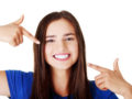 Beautiful woman in blue t-shirt pointing with her fingers at her perfect white teeth on white background