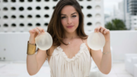 A girls in white dress holding the breast implants in her hands