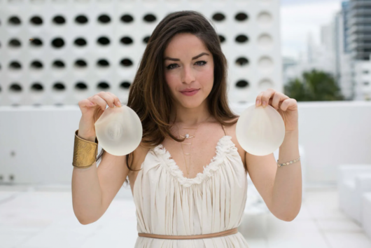 A girls in white dress holding the breast implants in her hands