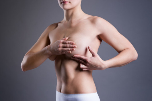 A girl covered her breast with a hand on a grey background