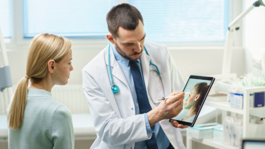 The girl is at consultation with the doctor who is showing what will be changed on girl's face after the plastic surgery