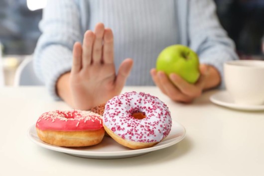 Girl holding a green apple and refuses to eat donuts 