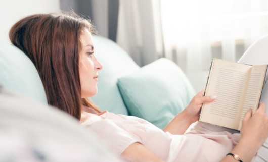 A girl resting in bed with a book at home after breast augmentation procedure