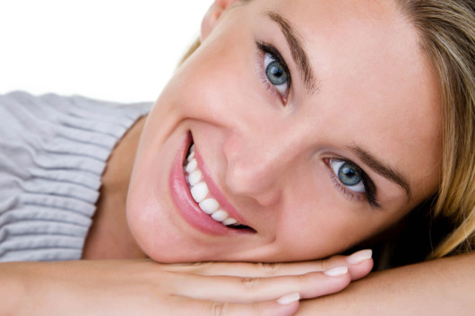 A girl on the white background shows her bright and straight teeth and beautiful smile. 