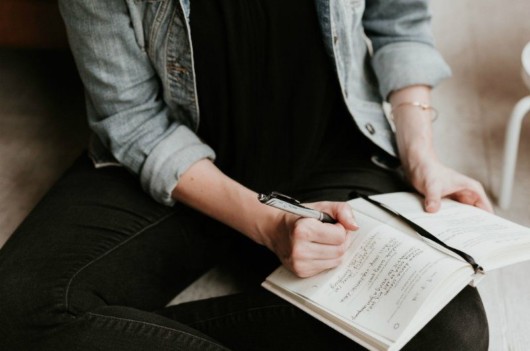 Guy in black jeans sitting on the floor with the note on his knee and writing down affirmations