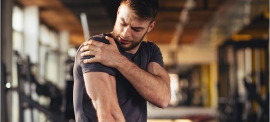 A man in a dark t-shirt holding her shoulder in pain