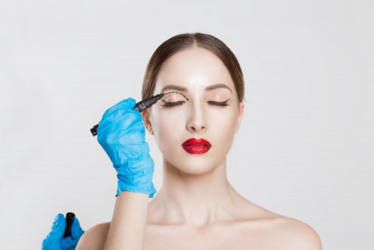 A doctor makes marks on the eyelid of a beautiful girl before cosmetic procedure