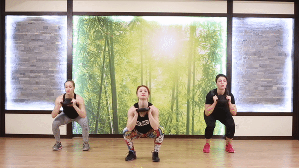 Three girls in sporty outfit doing squat to shoulder press exercise in the room. Girls performing fat blast workout