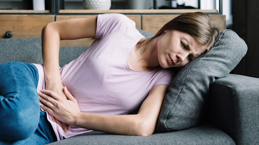 A girl in pink t-shirt and jeans lying on the sofa and holding her stomach in pain