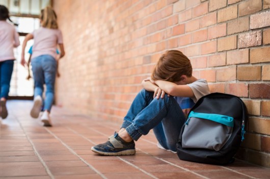 Abandoned child is sitting on the floor in the school with his head on his forearms