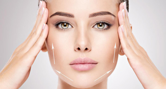 A close up face of a beautiful girl on the white background who touches her face with hands to show facelift