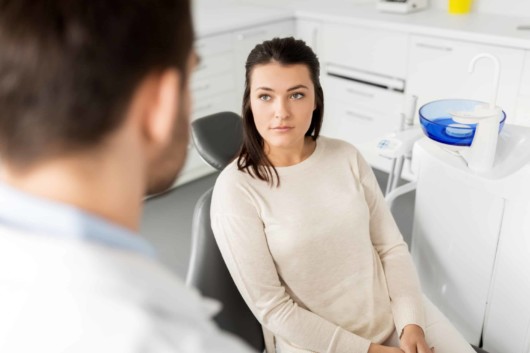 A beautiful girl is sitting in the chair at the dentist's and talking with the doctor before the dental procedure