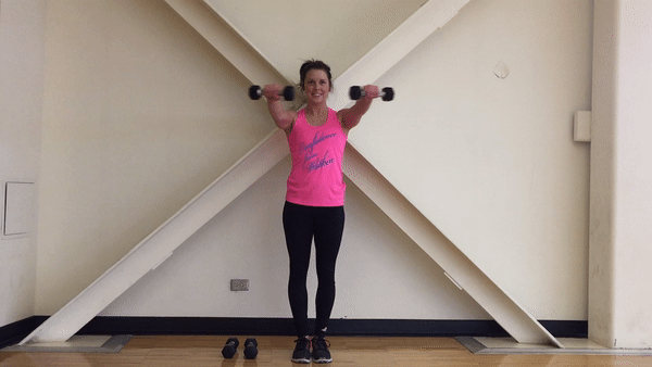 Fit girl in pinky sport t-shirt and black leggings is doing Dumbbell Front Raise to T Exercise. Girl is doing shoulder workout.