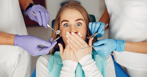The girl is lying in the dentist's chair covering her mouth with hands because she is afraid of dentists