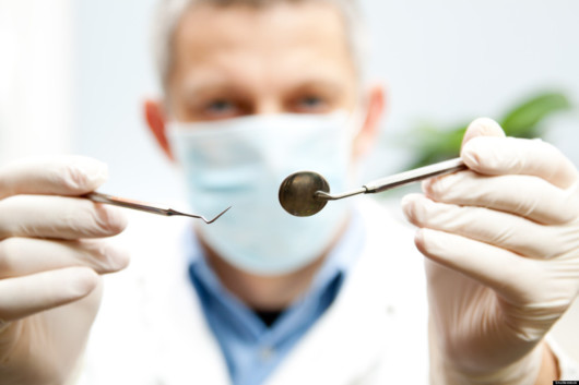 The doctor in face mask is trying to check the teeth with the dental instruments 