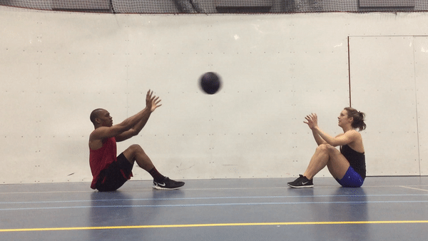 A fit couple is doing Long Medicine Ball Throws Exercise at the gym for strong abs and core