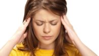 A beautiful girl in yellow sweater is touching her head with both hands trying to cope with dizziness