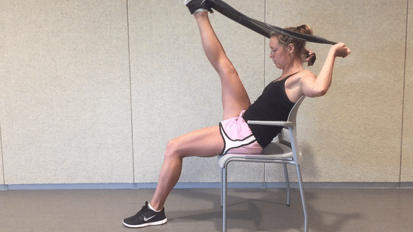 A fit girl in a black top and pinky shorts is sitting on the white chair in the room with the resistance band hands and doing Seated Resistance Band Hamstring Dynamic Stretch