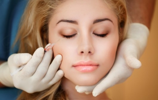 The doctor holds the injection near the girl's face before the cosmetic procedure