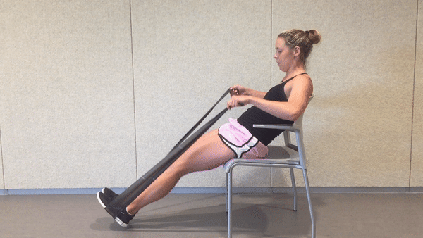 A fit girl in a black top and pinky shorts is sitting on the white chair in the room and doing Seated Resistance Band V-Sit ups
