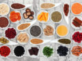 Different berries, vegetables, spices and greens are in white little plates and on white wooden background