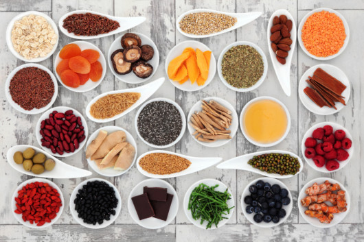 Different berries, vegetables, spices and greens are in white little plates and on white wooden background