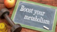 A black board on wooden background with the a sentence "boost your metabolism" written on it