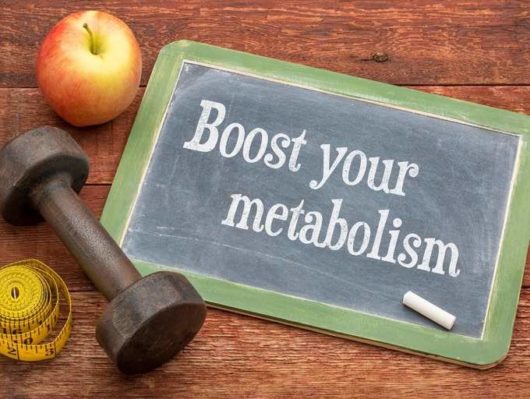 A black board on wooden background with the a sentence "boost your metabolism" written on it