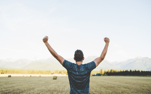 The man stands with his back and holds his arms up in the air showing his victory over drug addiction