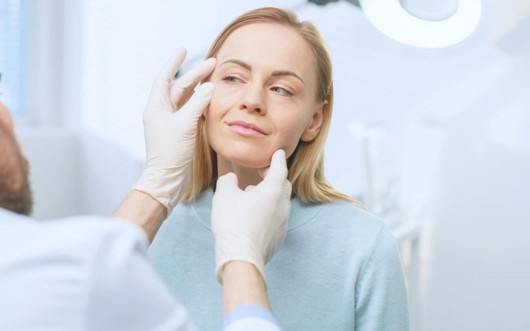 A woman has a  follow-up appointment with the doctor after the facelift procedure