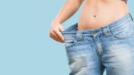Girl in blue oversized jeans on the blue background shows how much she removed fat with a popular cosmetic procedure