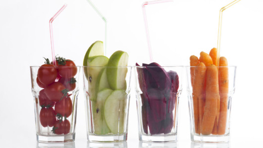 Four glasses filled with tomatoes, green apples, beetroot and carrots on white 