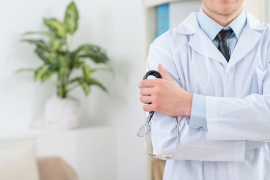 A doctor's torso in a white robe. He is holding stethoscope