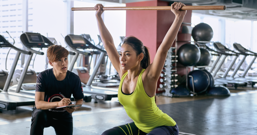 A personal trainer is checking the technique of her client white she is performing overhead squat