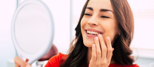 A beautiful girl is looking in the mirror, smiling an checking her dental implants