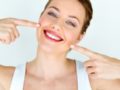 A beautiful girl on white background is smiling and pointing to her mouth and perfect white dental implants