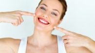 A beautiful girl on white background is smiling and pointing to her mouth and perfect white dental implants