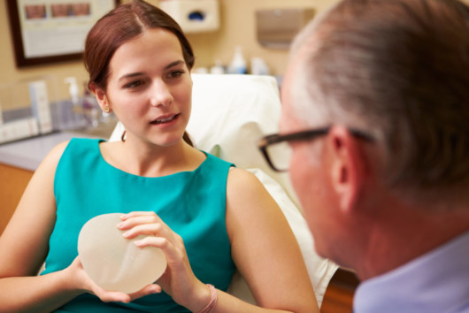 Girl is talking to the doctor and holding a breast implant before the breast augmentation