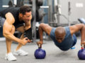 A personal trainer is motivating his client who is doing push ups on kettlebells