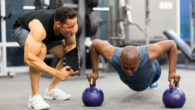 A personal trainer is motivating his client who is doing push ups on kettlebells