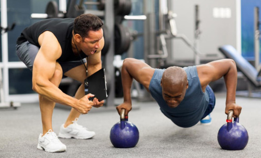 A personal trainer is motivating his client who is doing push ups on kettlebells