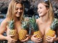 two girls covering their breasts with pineapples and smiling.