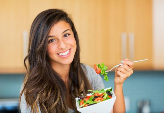 A girl holds a bowl of salad and smile