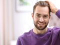 A man in purple sweater is touching his thick and beautiful hair after hair transplantation