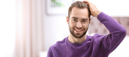 A man in purple sweater is touching his thick and beautiful hair after hair transplantation