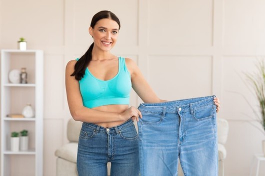 smiling girl who holds bigger jeans showing how she got slim