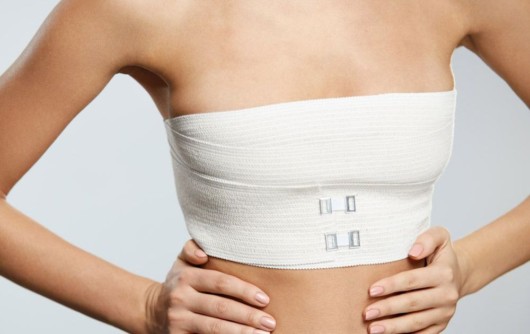 An isolated girl's body on white who is standing in gauze and compression garments after  breast reconstruction surgery  