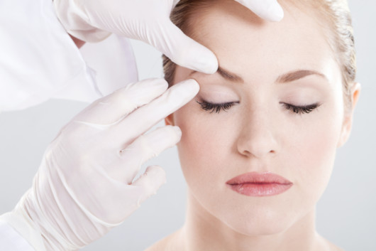 A close up face of a beautiful girl on white background and doctor's hands in white gloves 