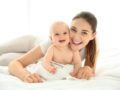 A happy mommy and a baby smiling and lying on the bed