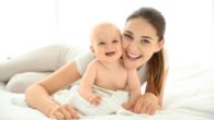 A happy mommy and a baby smiling and lying on the bed